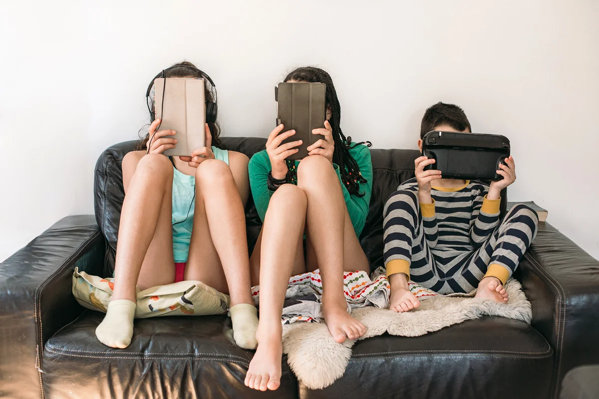 three kids with electronic devices on a sofa