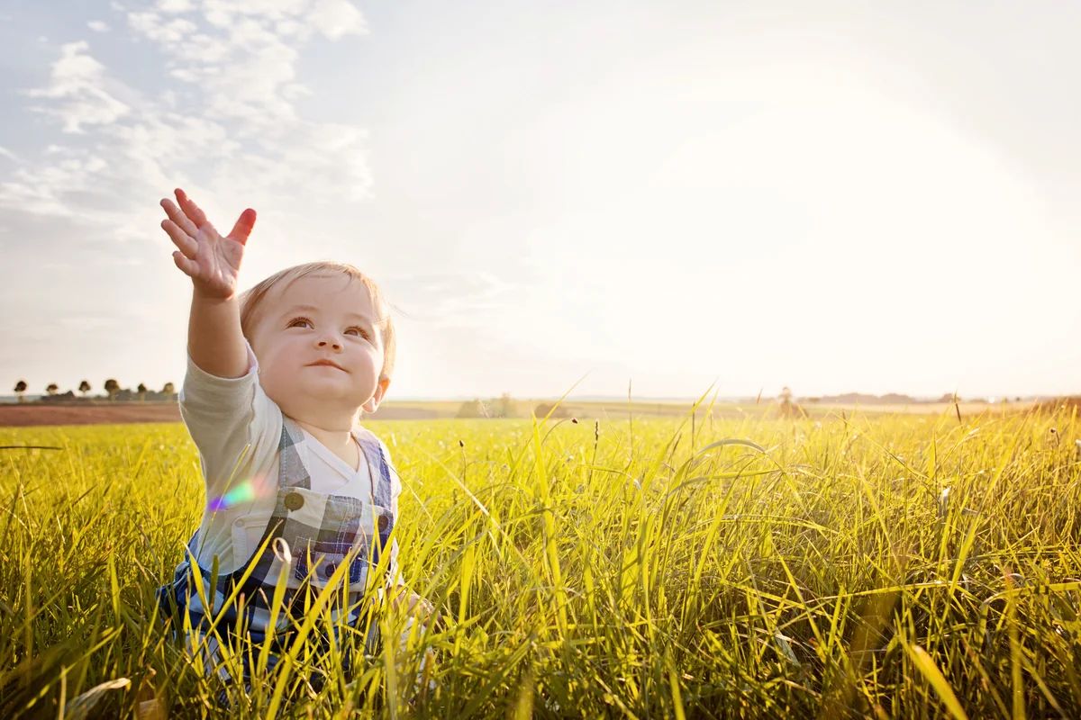 Baby sitting in Grass reaching to the Sky