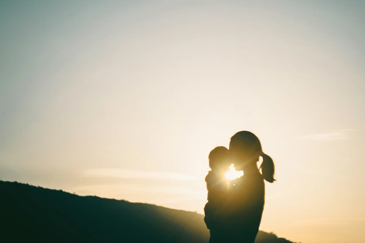 Silhouette of mother carrying baby girl outdoors against sky