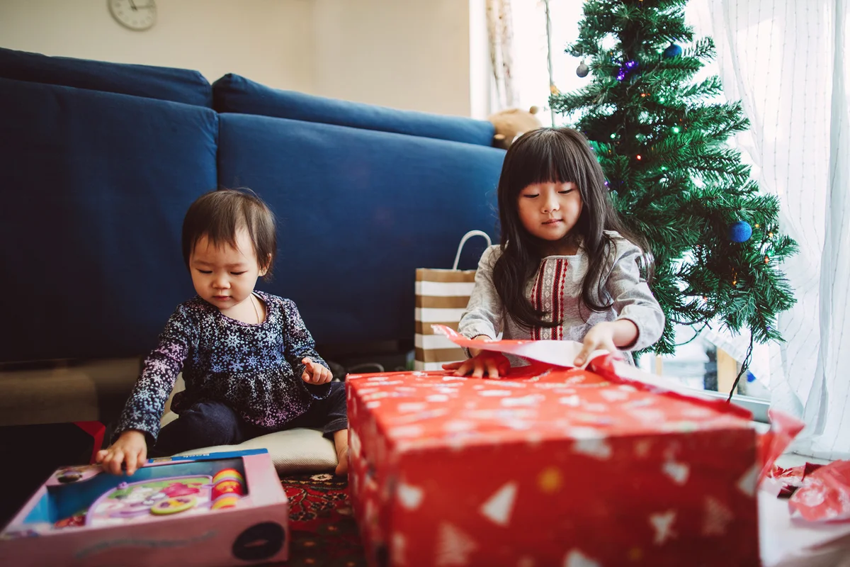 lovely little girl opening Christmas presents with her little baby sister at home