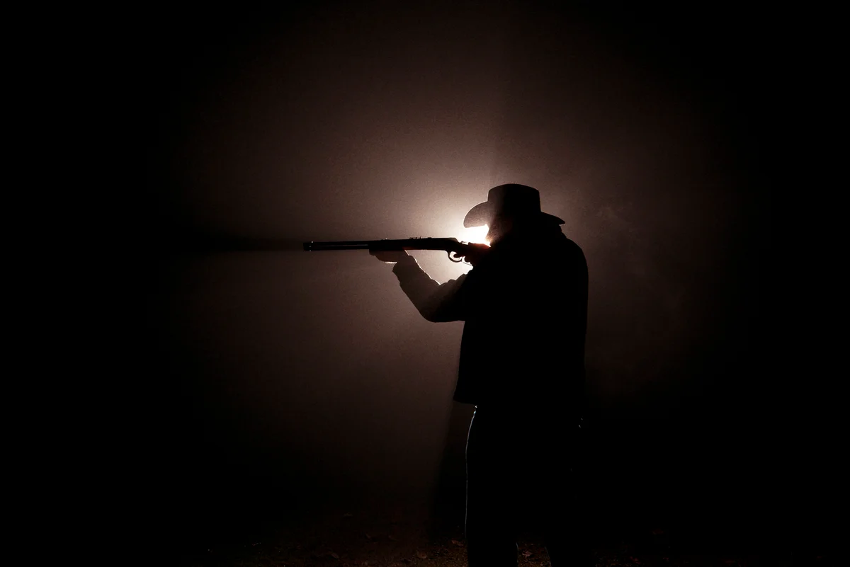 Dark silhouette of a cowboy in a Stetson shooting his gun