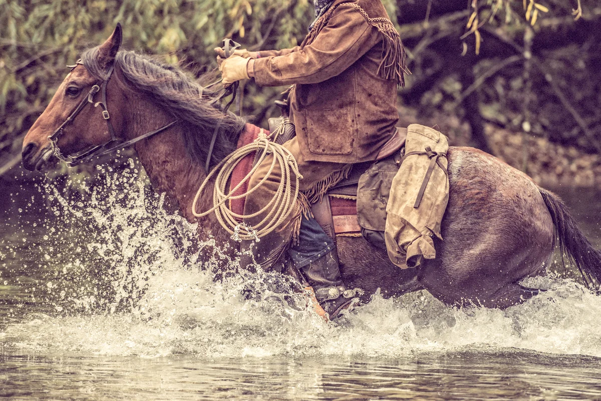 Cowboy on a horse riding across a river