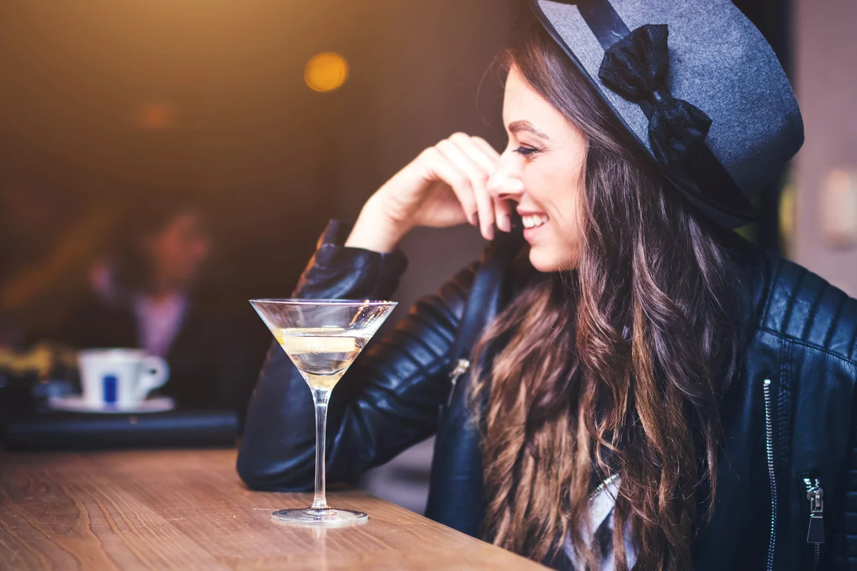 Young brunette woman sitting at a bar and enjoying a cocktail with a lemon twist