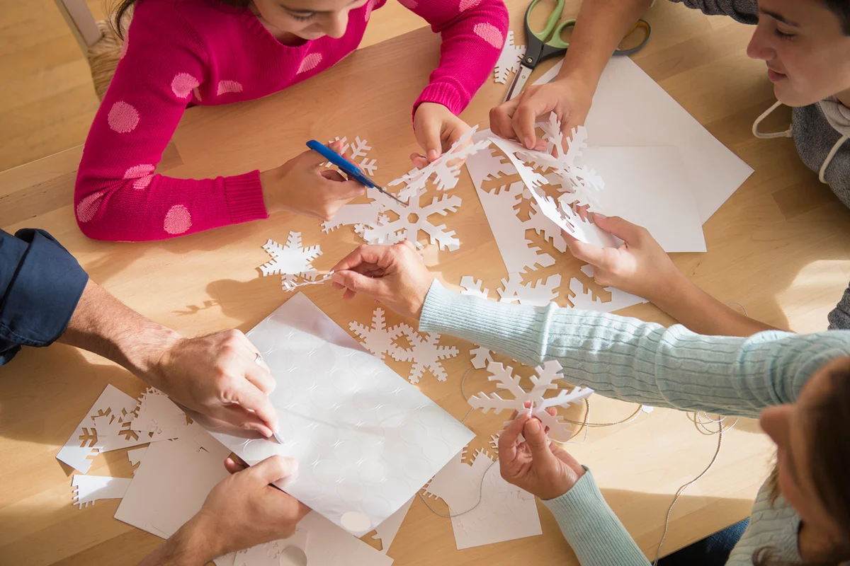 Classmates cutting out paper snowflakes with teacher
