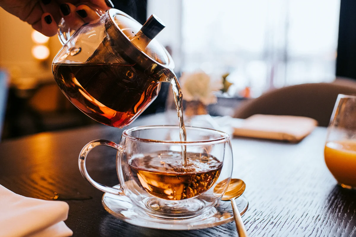Hand pouring a cup of tea from a stylish transparent teapot