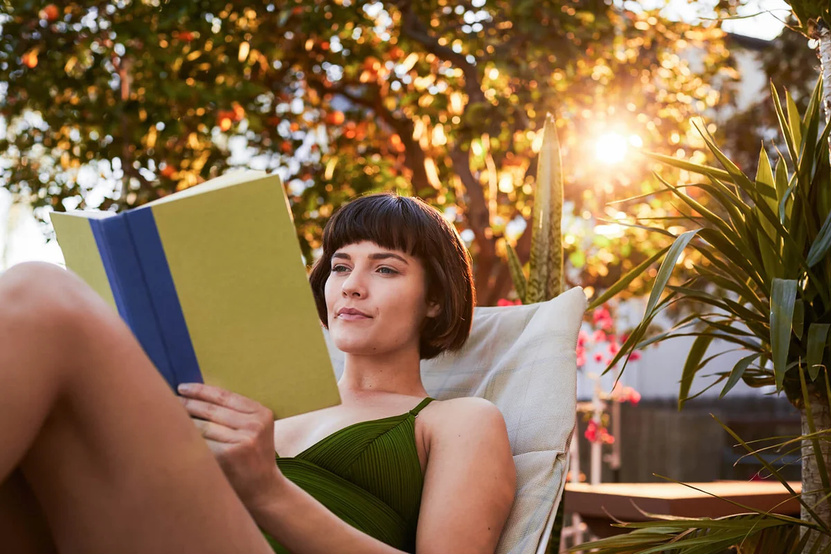 Young woman in a swimsuit reading a book on her patio