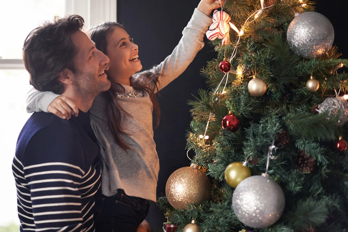young girl and her father decorating the Christmas tree together