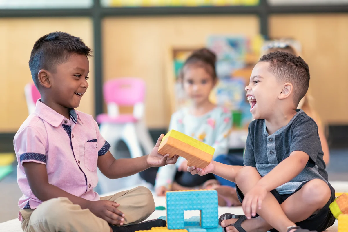 Happy preschool students playing together and sharing in classroom