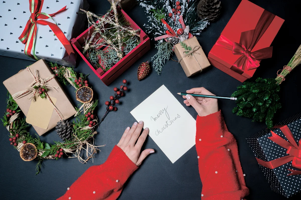 Christmas decorations and presents with a hand writing a Christmas card