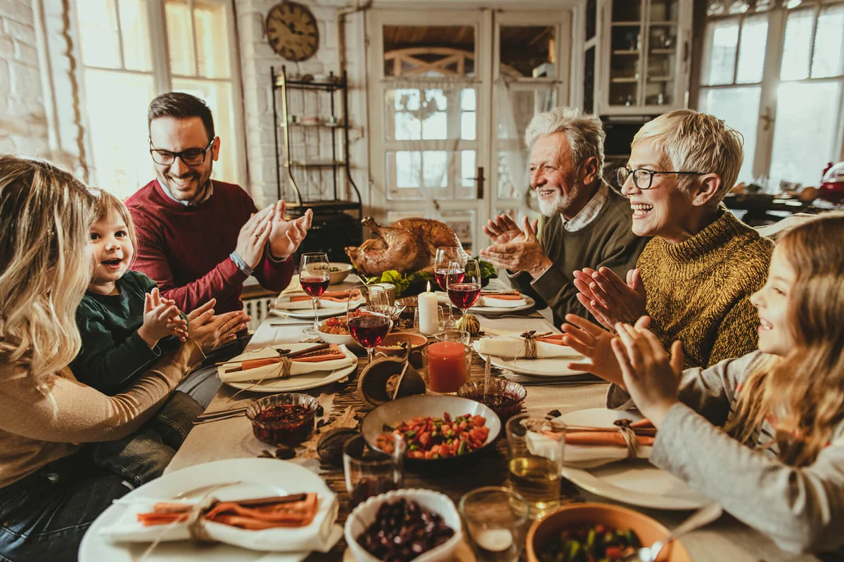 Happy extended family applauding during Thanksgiving meal at dining table
