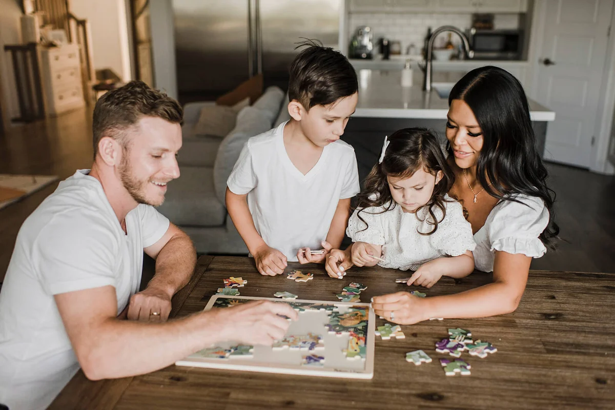 Smiling parents solving puzzle with kids over table at home