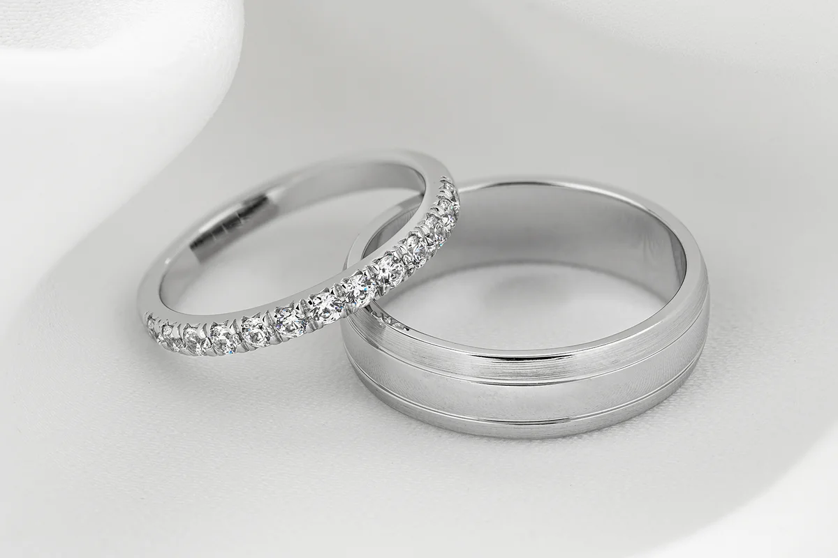Pair of modern white gold wedding ring bands with diamonds on female ring.