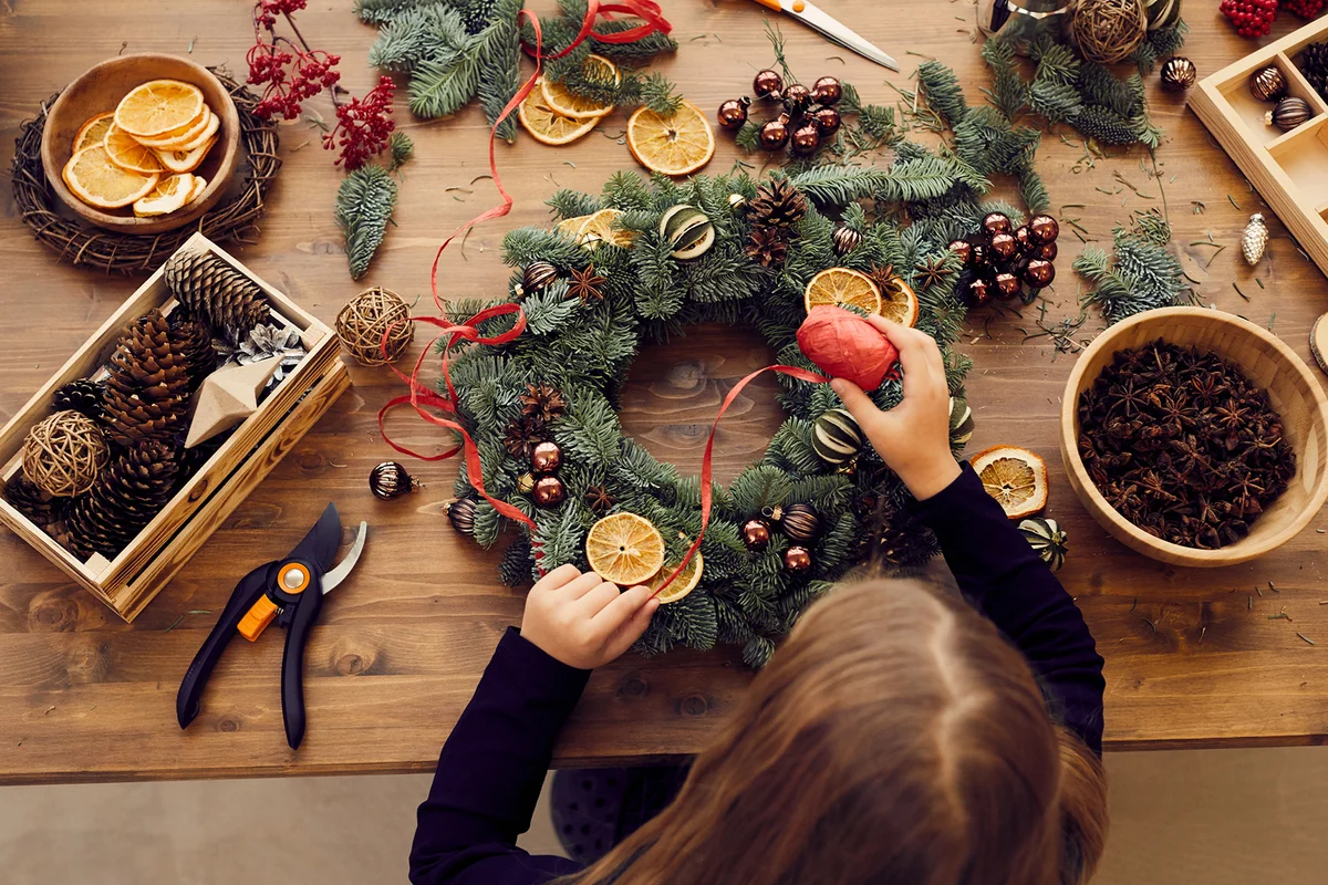 woman standing at desk and using decorative ribbon while making Christmas wreath