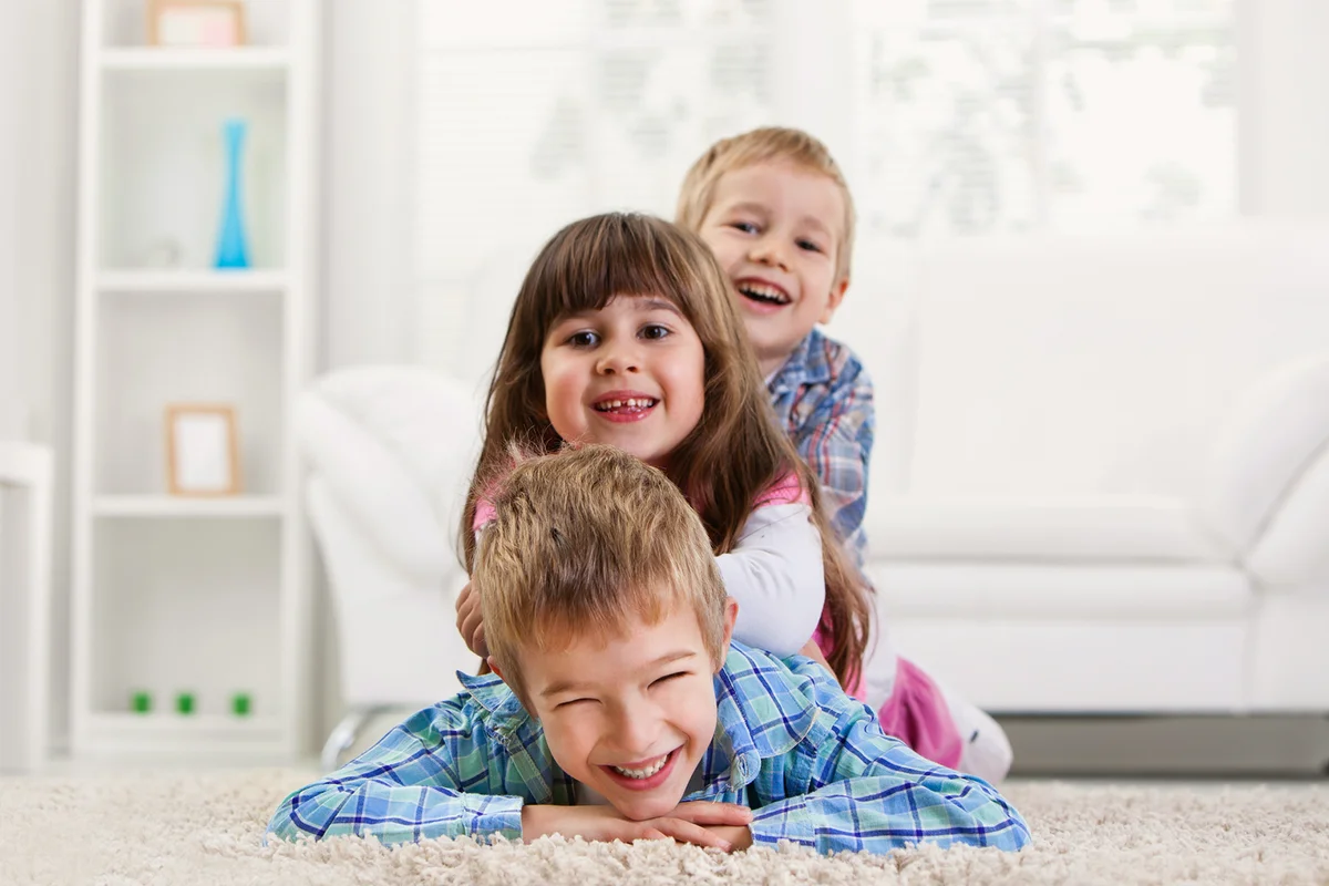Three siblings lying down on the floor in livingroom.