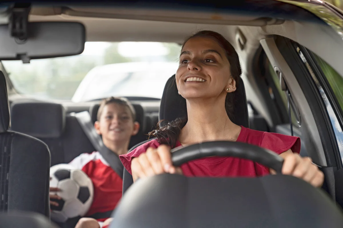 Happy soccer mom transporting kid to football practice in her car