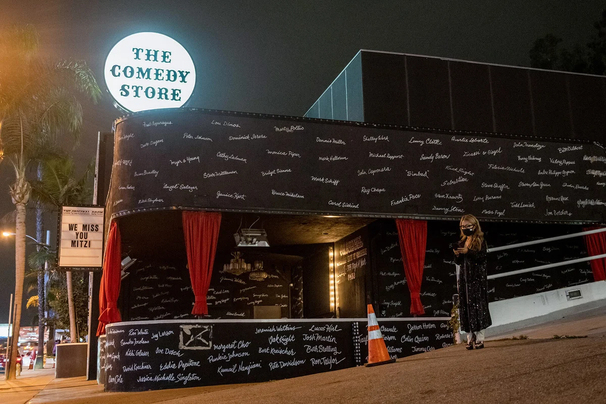 A woman wearing a mask the stands outside The Comedy Store at night along Sunset Boulevard | Getty Editorial Use