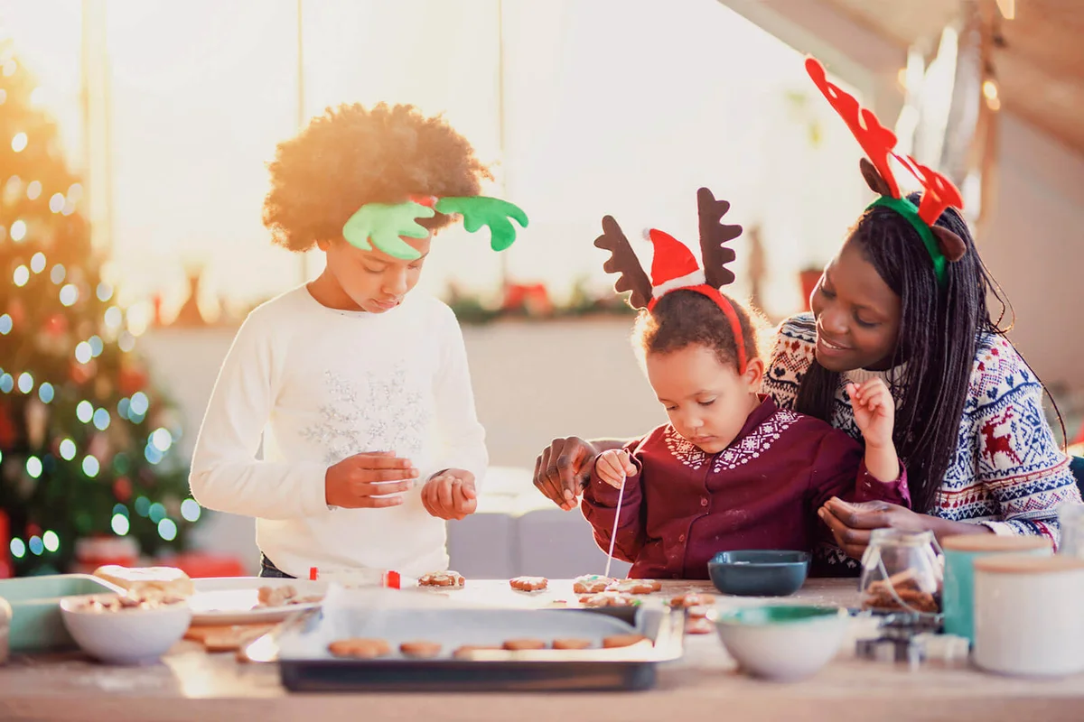 Smiling mother enjoying decorating Christmas cookies with her cute daughters for Christmas