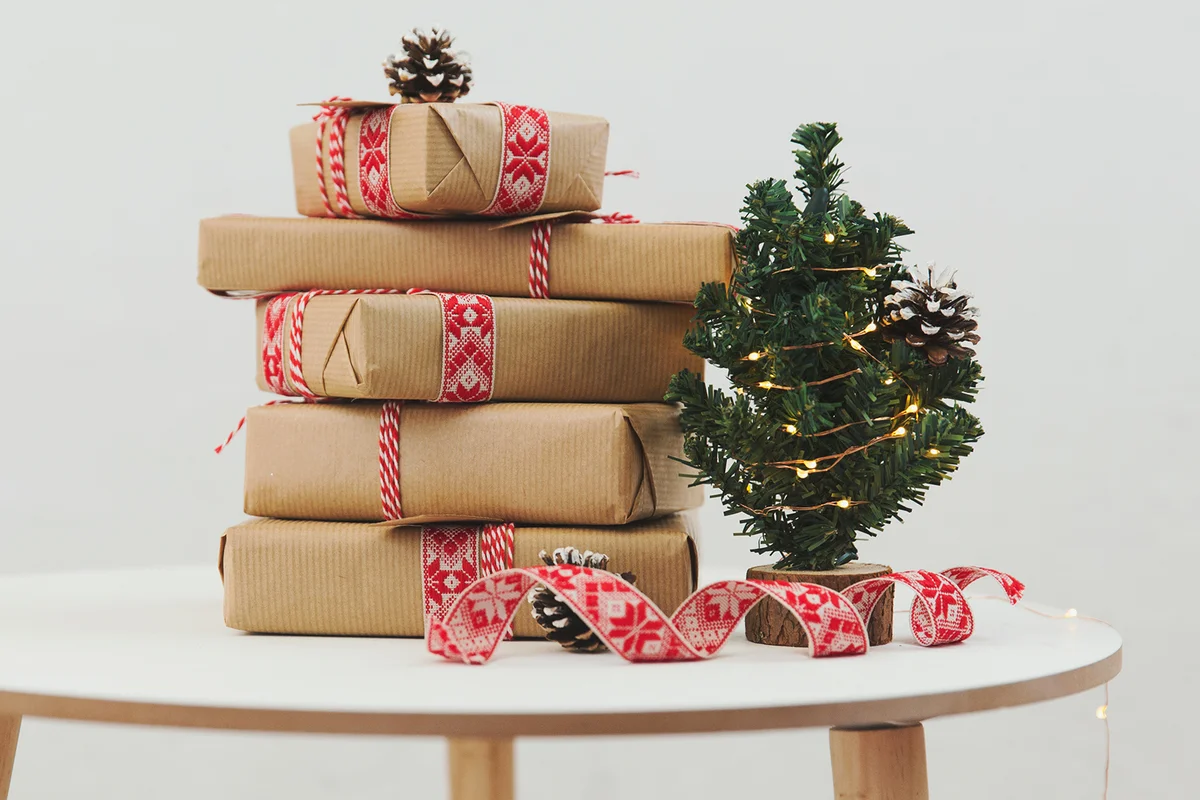 Stack of wrapped Christmas gifts next to a miniature Christmas tree