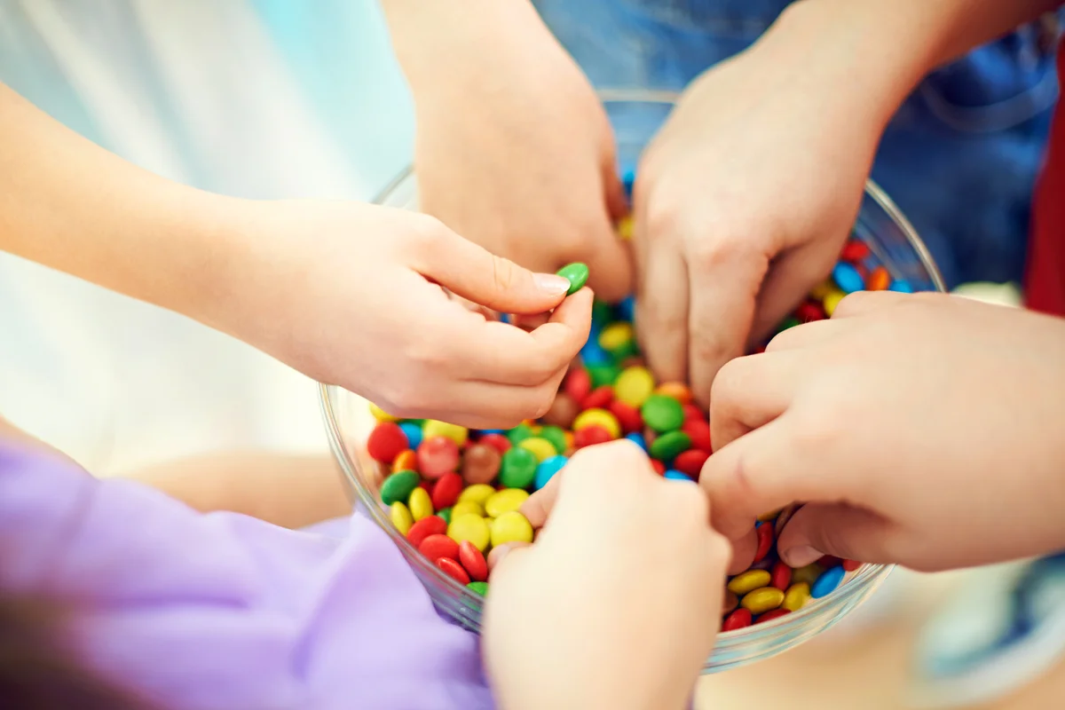 Hands of kids taking multi colored chocolate candies from bowl