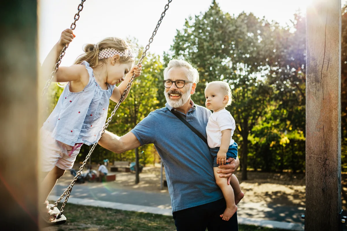 Grandfather Having Fun With Grandchildren On Swings