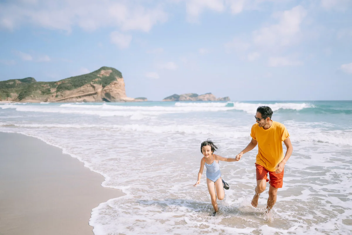 Father and daughter playing in waves on beach