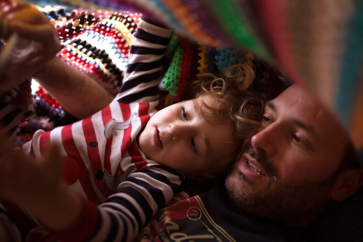 Dad and kid under a colorful blanket