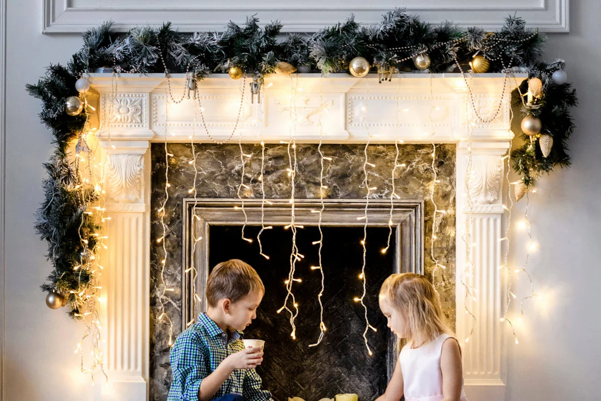 Boy and his little sister sitting together in front of fireplace at Christmas time