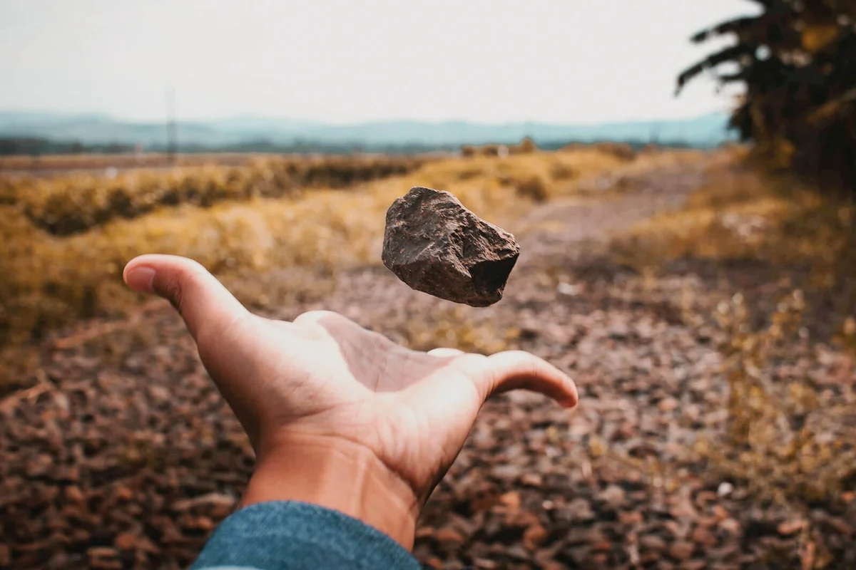 Cropped Hand Of Man Tossing Stone On Field