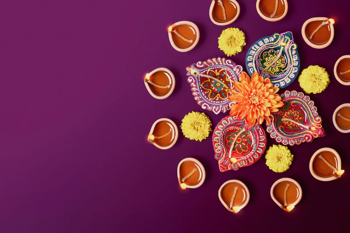 Colorful clay diya lamps with flowers on purple background
