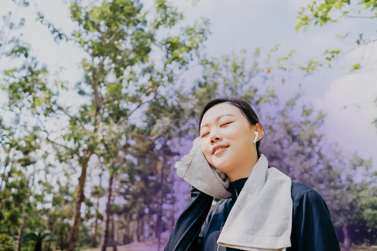 Young woman after exercising and wipe the face with towel in public park