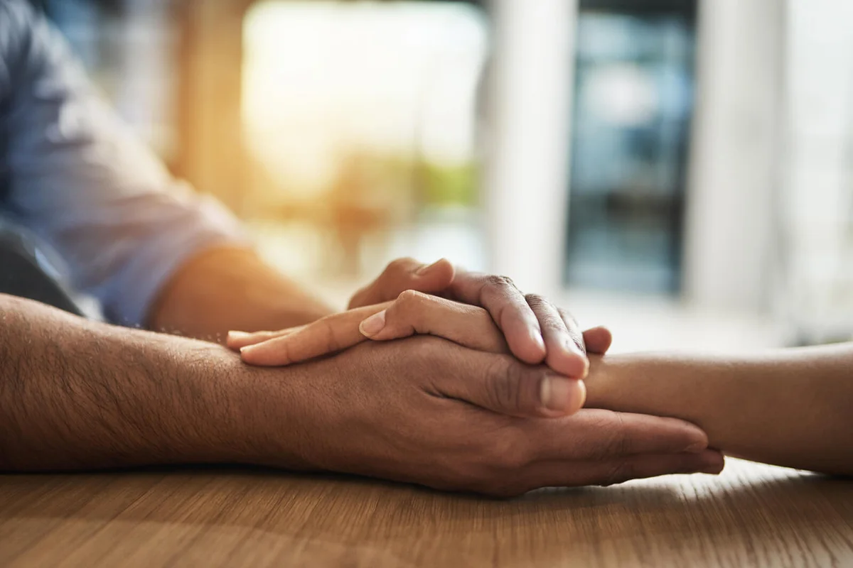 man and woman compassionately holding hands at a table