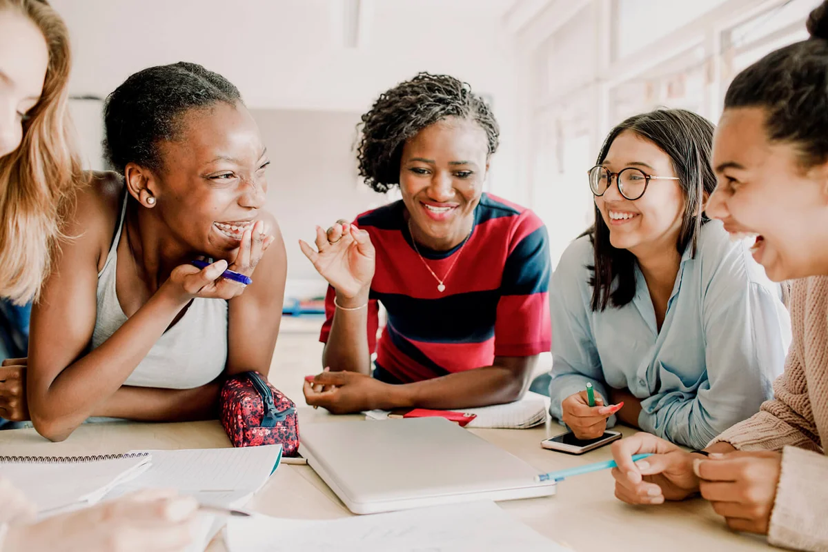 Smiling teacher gesturing while cheerful students sitting by table in classroom
