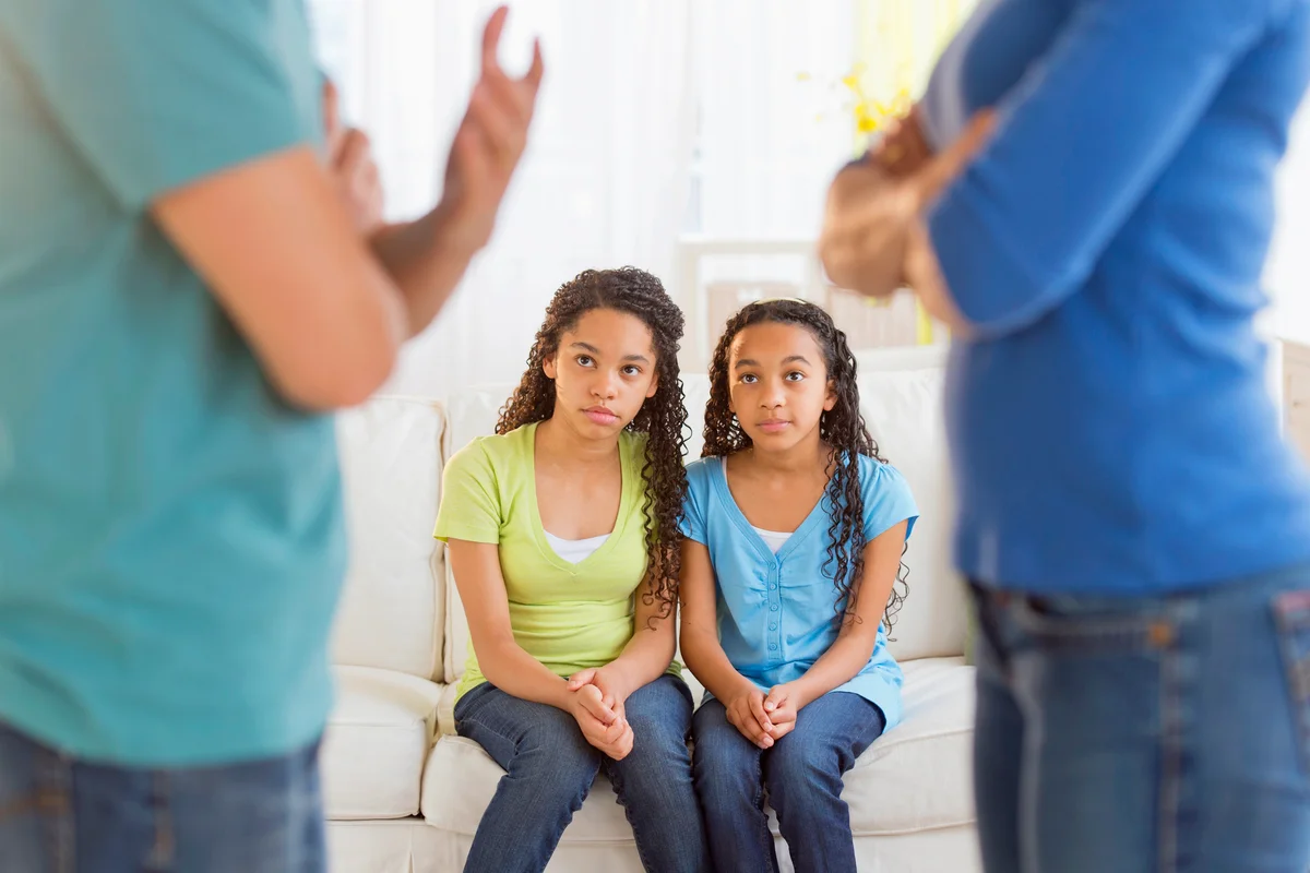 Parents quarreling, with daughters sitting on the couch