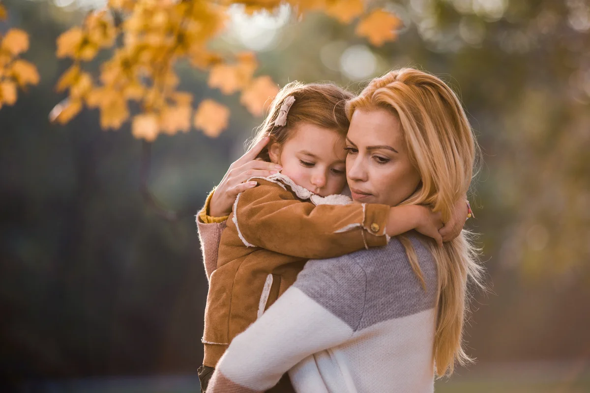 Affectionate mother consoling her little girl during autumn day in nature