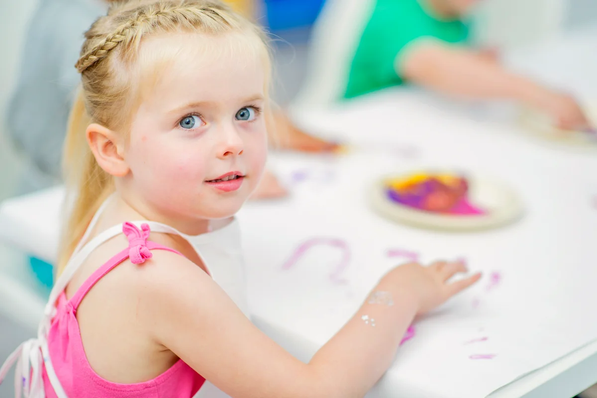 A young girl is sitting at a table finger painting