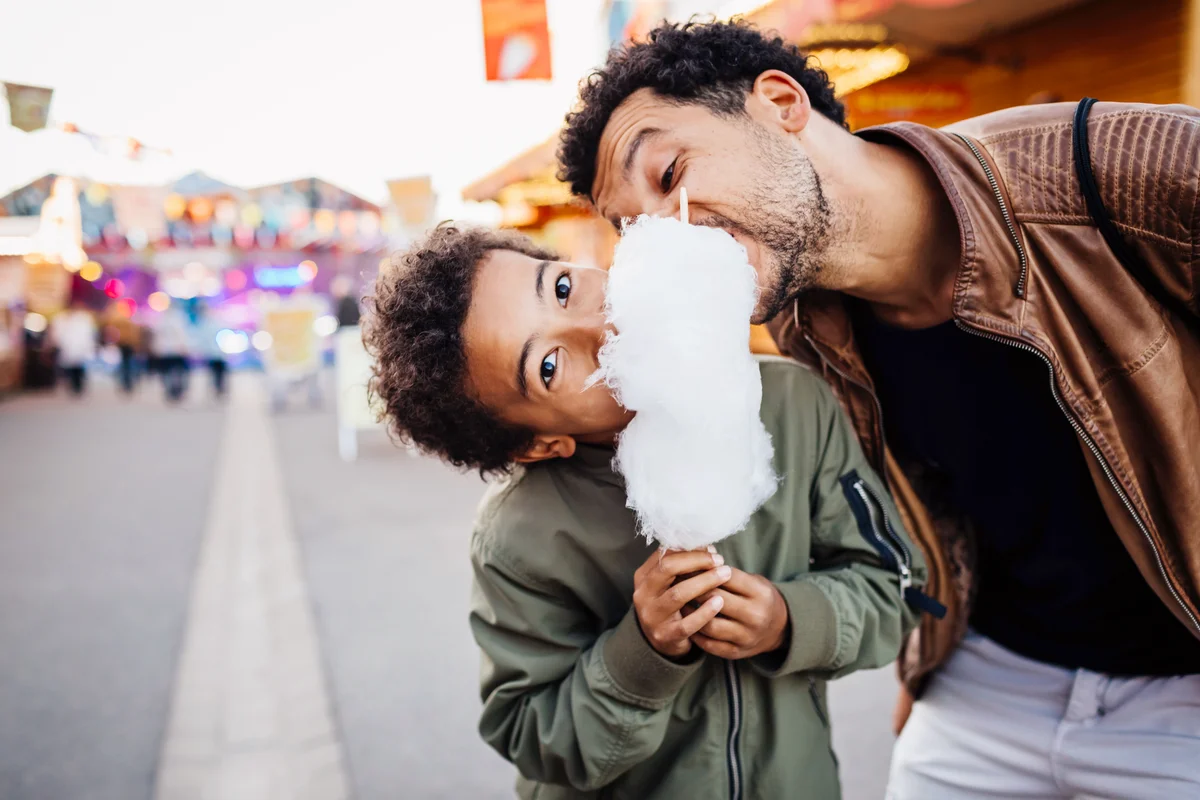 Playful father and son sharing candy floss at the fun fair