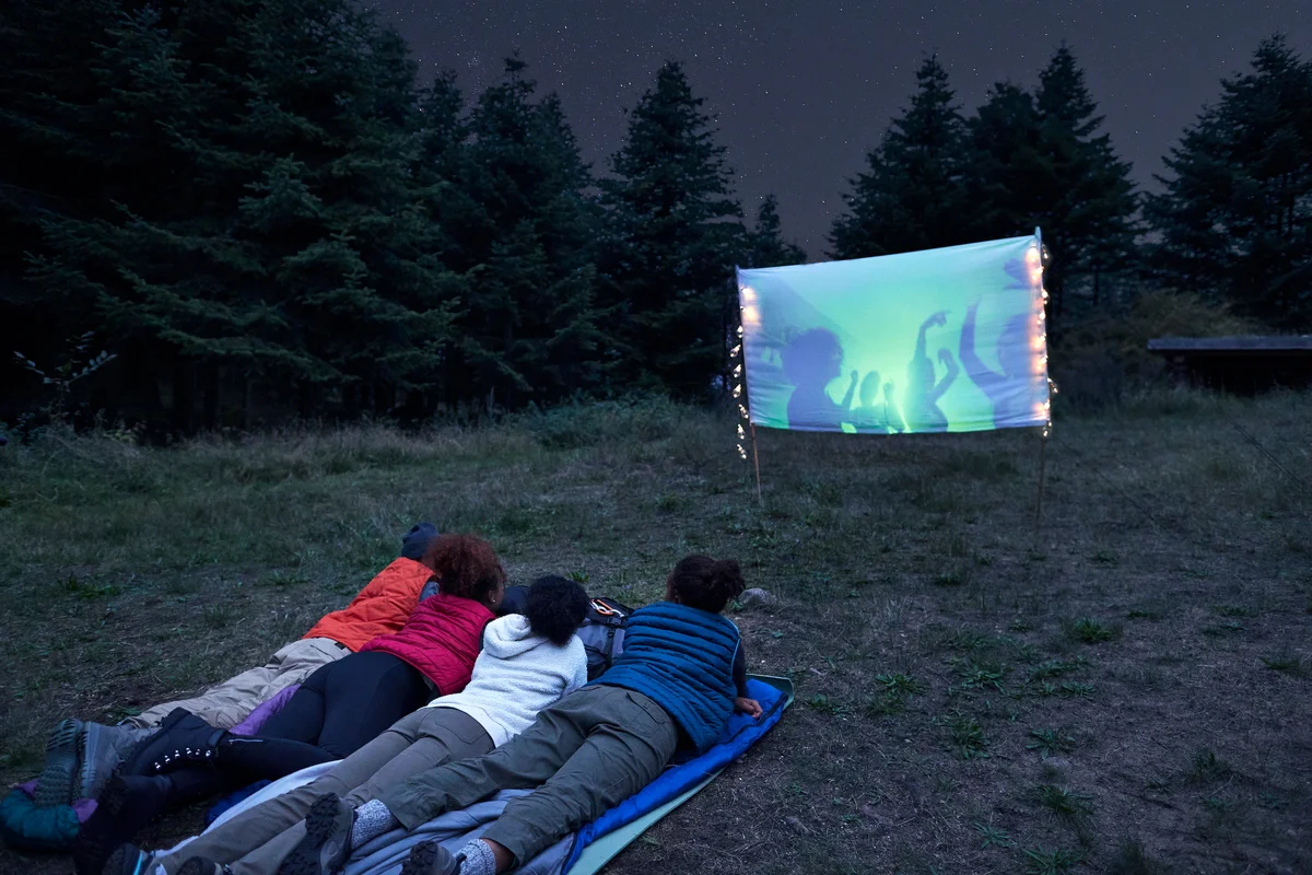 Young friends watching projection screen at campsite during night