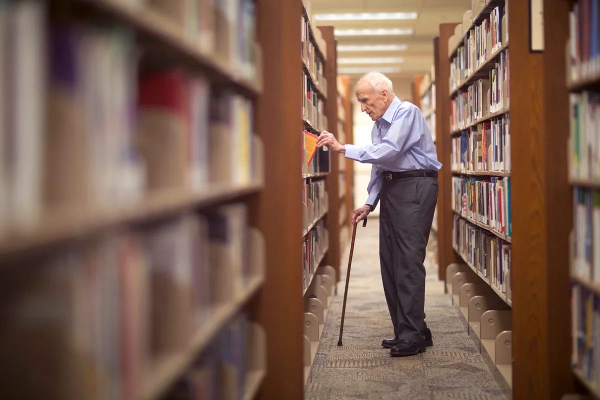 Senior man looks through books in a library