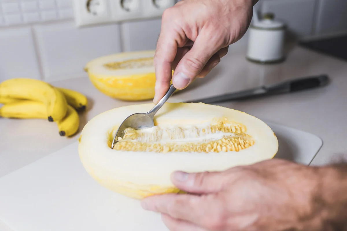 A man using a spoon takes out a ripe melon seeds
