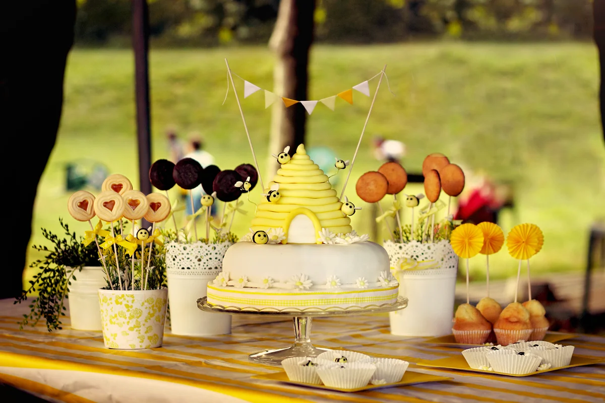 Candies, cookies, cupcakes and a cake shaped as a honeycomb with fondant bees flying and yellow cute little flags.