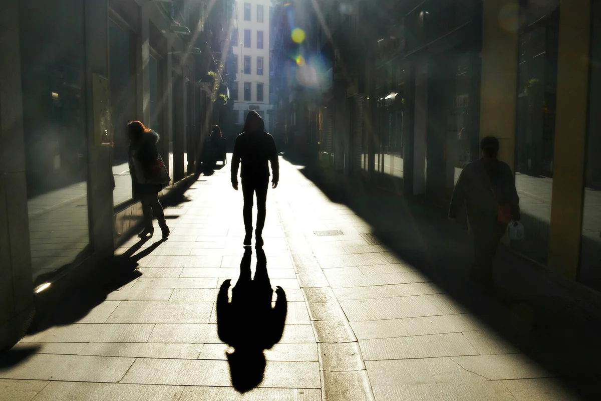 Man and his shadow walking towards the camera backlit by and in high key light