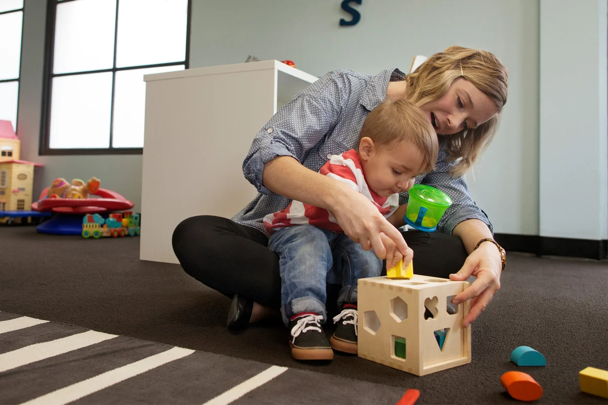 Baby sitter and boy playing with geometric puzzle box