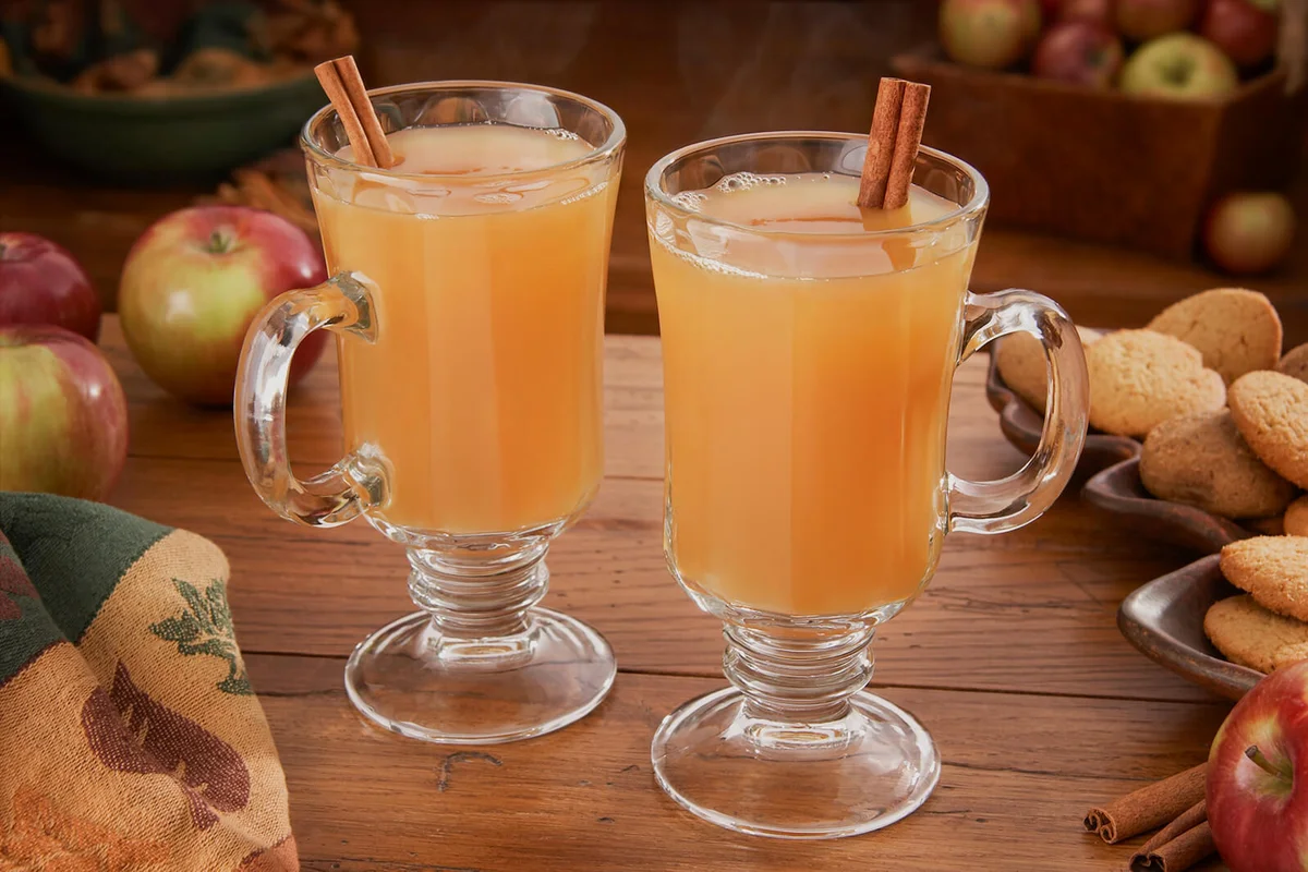 Steaming hot apple cider on a table with apples and ginger cookies