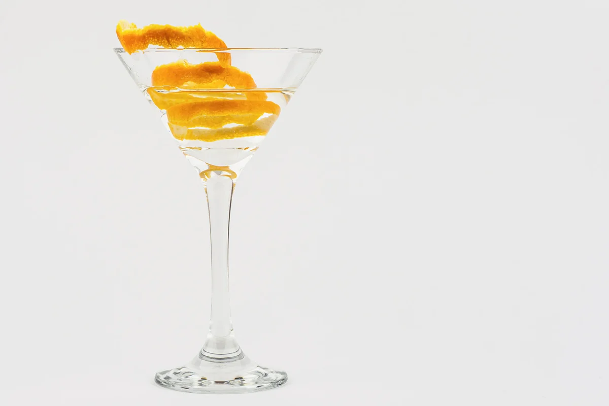 Cocktail in a triangular glass cup with orange fruit peel