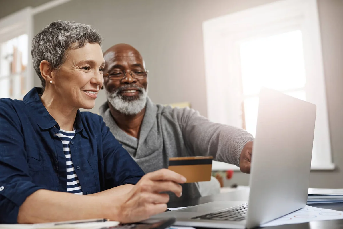 senior couple using a credit and laptop while working on their finances at home