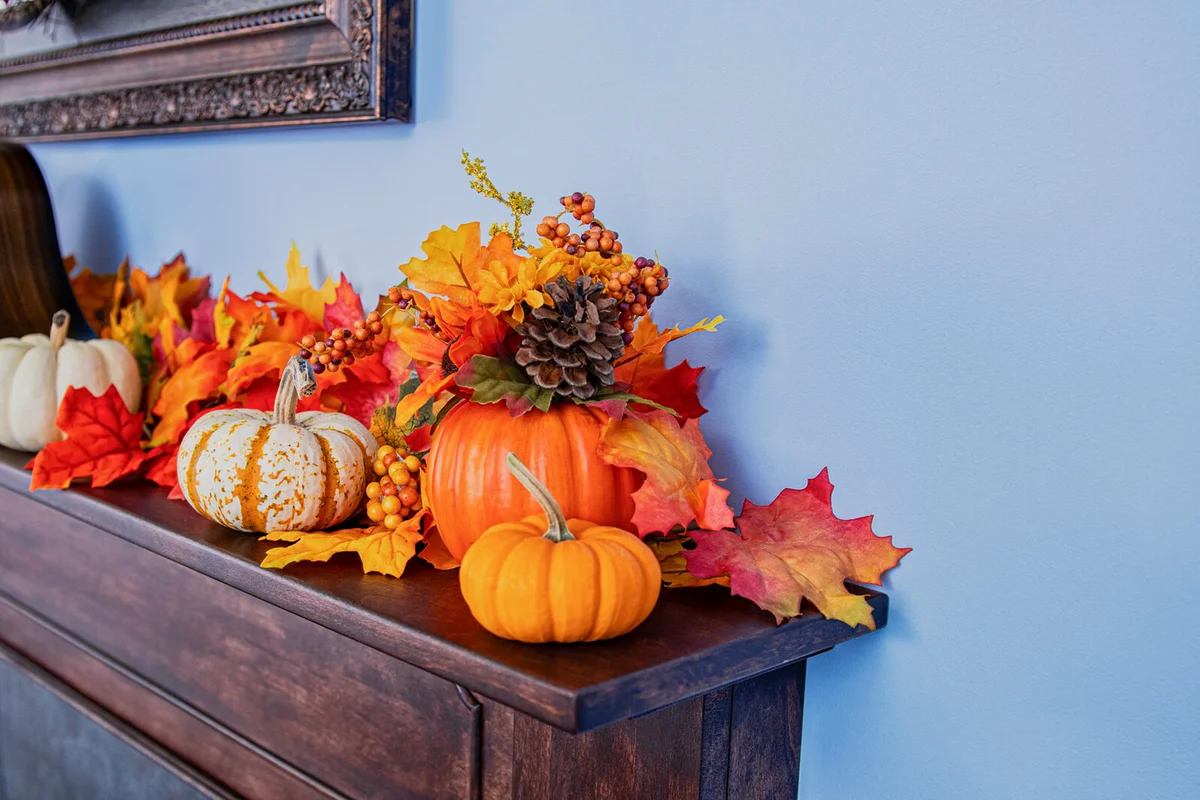 Fall decorations of pumpkins, silk leaves and flowers on fireplace mantel