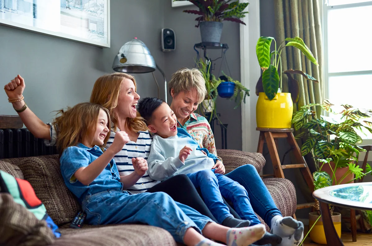 Cheerful family with two mums watching tv at home