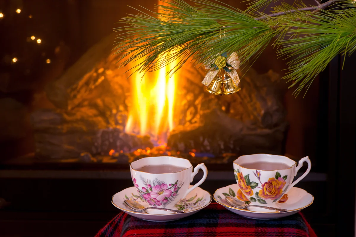 Antique teacups on tartan pattern scarf under Christmas tree in front of fireplace