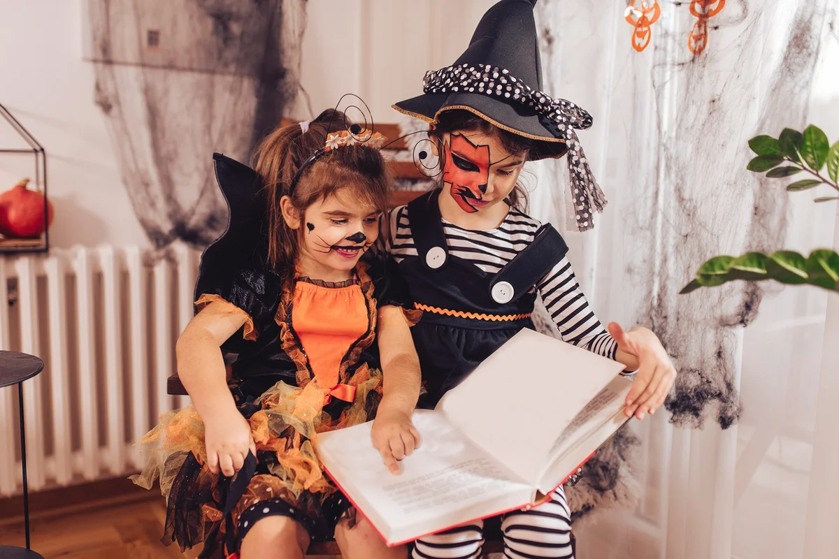 Two cute sisters reading spooky fairy tales for Halloween at home