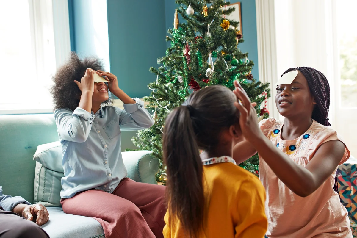 Sisters sticking adhesive notes on forehead while sitting in living room at home